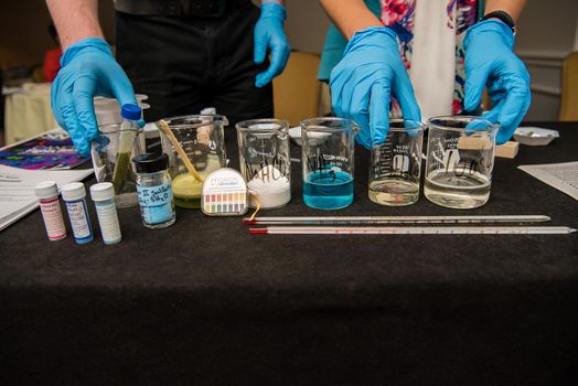 A close up of science experiment materials including colorful liquid filled beakers and various vials and stirring mechanisms.