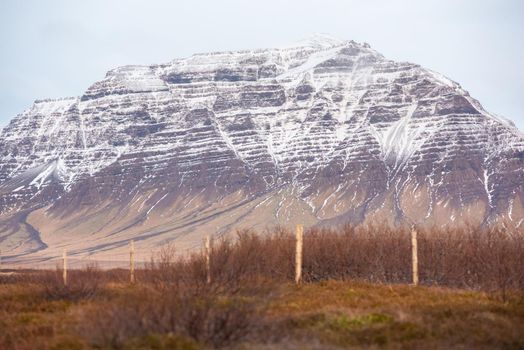 Colorful snow capped mountain showing off geological textures and layers Icelandic landscape with fence line