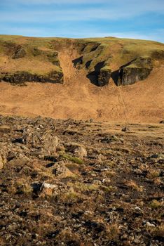 Vertical image of Icelandic topography with warm brown and orange tones and rocky texture with a blue sky