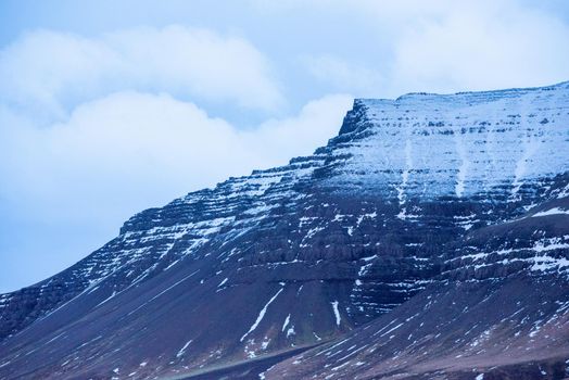 Close up of snow capped black mountain ridges in Iceland with clouds to add depth.