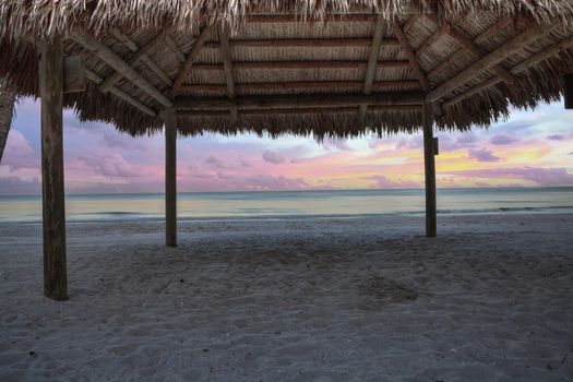 Sunrise over tiki hut on the ocean at Port Royal Beach in Naples, Florida.