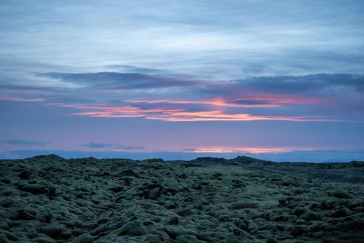 Icelandic landscape photo at sunset with volcanic rock field covered in green moss with a pretty purple and pink sky