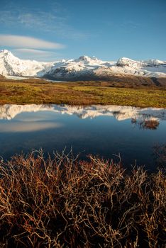 Icelandic mountain range with beautiful snowcapped mountains reflected into still water.