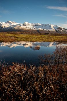 Icelandic mountain range with beautiful snowcapped mountains reflected into still water.