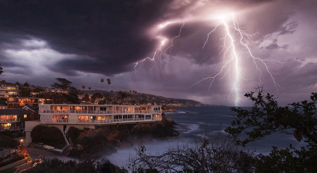 Lightning flashes over a cliff overlooking the ocean in Laguna Beach, California at sunrise.