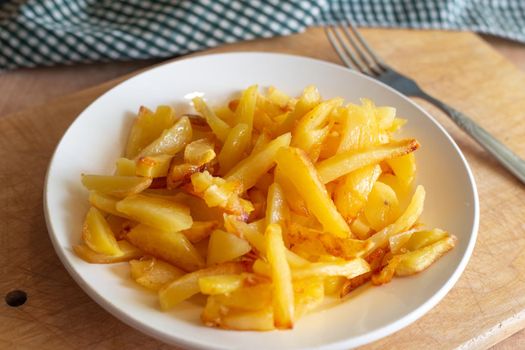 Fresh golden fried potatoes in a white plate on a wooden stand. Delicious vegetable dish.