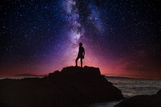 Night stars over Man’s reflection silhouette at the ocean water as it cascades over rocks in Reykjavik, Iceland.