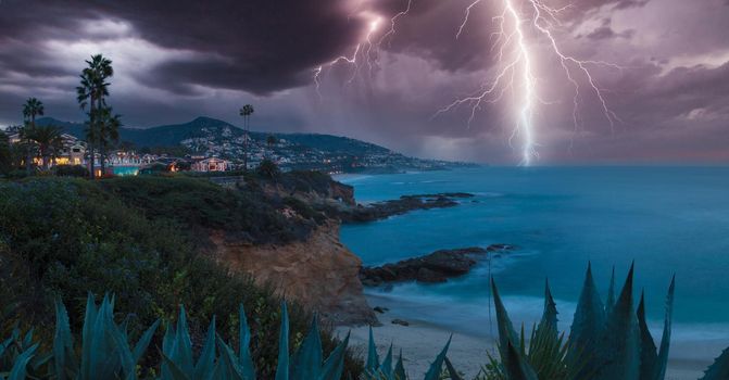 Lightning flashes over a cliff overlooking the ocean in Laguna Beach, California at sunrise.