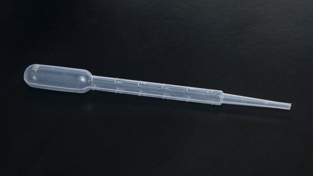 Big plastic dropper on a black background close up