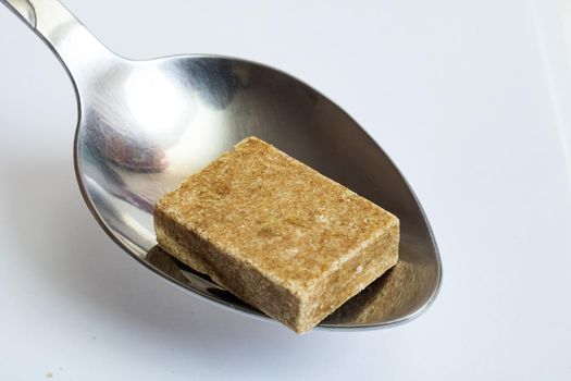 Yellow bouillon cube in a spoon close up