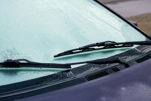 The icy windshield of a black car close up