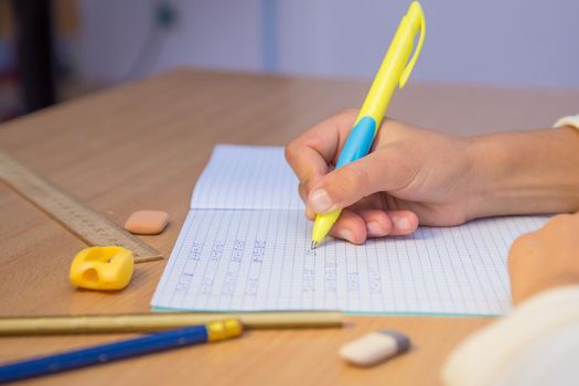 Pupil's hand writes with a ballpoint pen in a notebook close-up. A schoolboy performs a task at the workplace. The concept of children's education, teaching knowledge, skills and abilities.