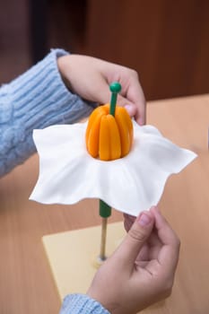 The pupil's hands are holding a close-up of a flower model. A schoolboy performs a task at the workplace. The concept of children's education, teaching knowledge, skills and abilities.
