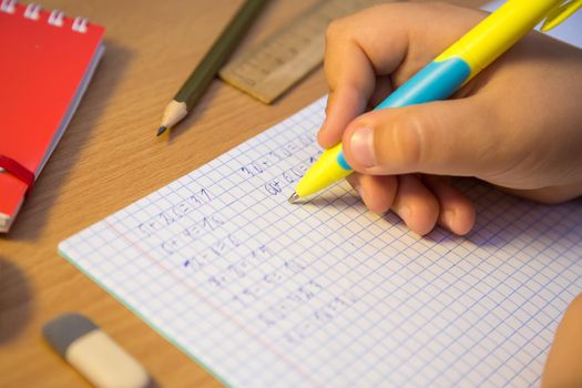 Pupil's hand solves math examples with a ballpoint pen close-up. A schoolboy performs a task at the workplace. The concept of children's education, teaching knowledge, skills and abilities.