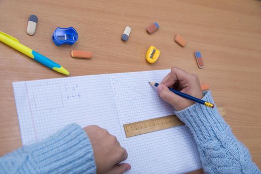 The student in the notebook signs the notation with a pencil. A schoolboy performs a task at the workplace. The concept of children's education, teaching knowledge, skills and abilities.