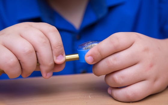 Close-up hands of a student turn a pencil in a sharpener. A schoolboy performs a task at the workplace. The concept of children's education, teaching knowledge, skills and abilities.