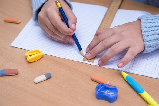 A student in a notebook draws a geometric figure with a pencil. A schoolboy performs a task at the workplace. The concept of children's education, teaching knowledge, skills and abilities.