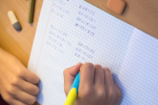 Close-up pupil's hand solves math examples in a notebook. A schoolboy performs a task at the workplace. The concept of children's education, teaching knowledge, skills and abilities.