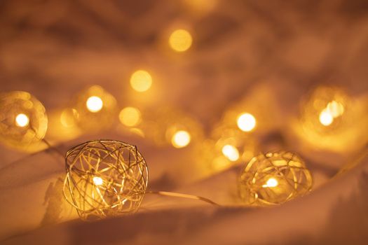 Close up shot of golden blurred Christmas lights on rumpled bed sheets, making cozy and romantic atmosphere. Festive bokeh background with lights.
