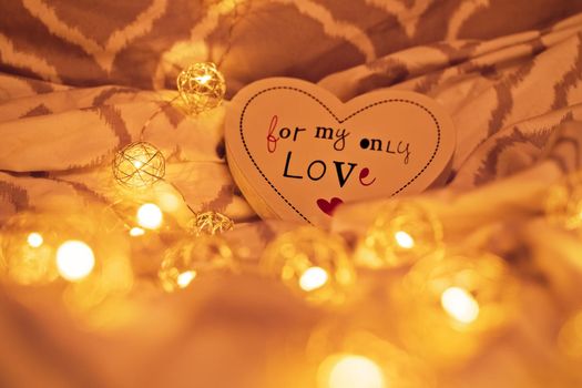 Cosy, warm, and romantic atmosphere on bed sheets. Heart shaped decoration and golden blurred Christmas lights on bed sheet. Valentine's Day and Wedding Day concept. Love and marriage concept.