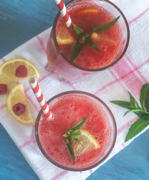 Fresh watermelon juice with raspberries and lemon in a glass. Slices of lemon and raspberry on the table. Top view. The concept of natural nutrition.