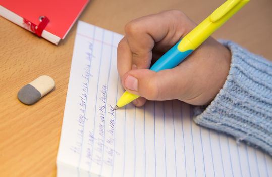 Close-up pupil's hands are writing in English with a ballpoint pen. A schoolboy performs a task at the workplace. The concept of children's education, teaching knowledge, skills and abilities.