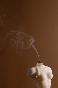 Candle in woman torso shape burning in brown interior , atmosphere and smoke after candle side view