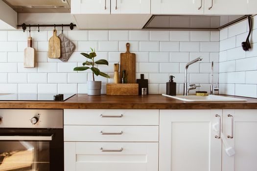 Kitchen brass utensils, chef accessories. Hanging kitchen with white tiles wall and wood tabletop.Green plant on kitchen background side view