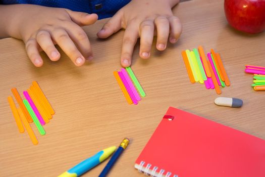 The student's hands are counted as multi-colored sticks close-up. A schoolboy performs a task at the workplace. The concept of children's education, teaching knowledge, skills and abilities.