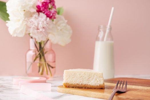 Homemade cheesecake and milk . French dessert and flowers on marble table on pink background side view