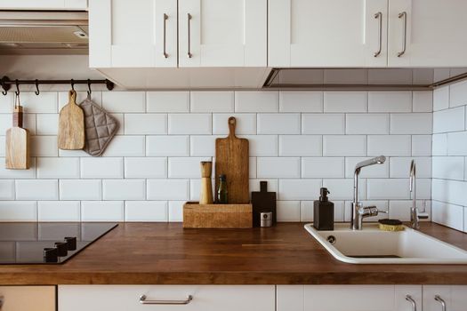 Kitchen brass utensils, chef accessories. Hanging kitchen with white tiles wall and wood tabletop.Kitchen background side view