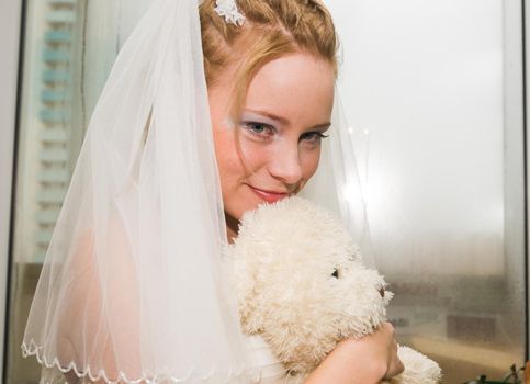 Young bride posing with teddy bear before wedding ceremony