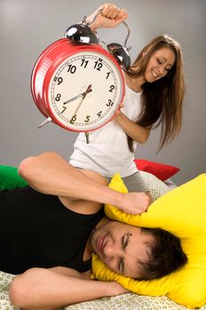 Beautiful Young couple sleeping in bed in the morning. Sleepy boyfriend waking up with alarm clock.