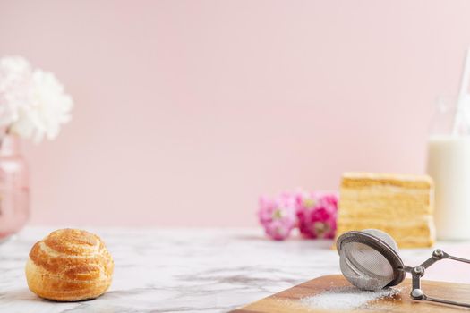 Homemade profitroles pastry filled with custard. Eclairs with cream, French dessert and flowers on marble table on pink background side view