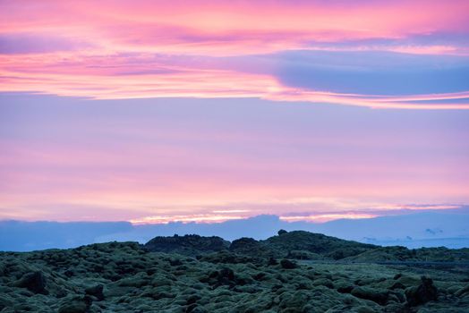 Icelandic landscape photo at sunset with volcanic rock field covered in green moss with a pretty purple and pink sky