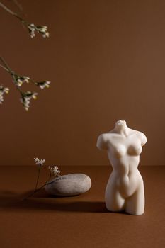Candle in woman torso shape in brown interior with stone and dried flowers, autumn atmosphere vertical