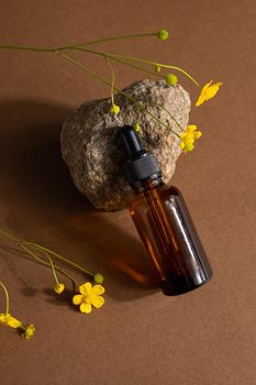 Brown glass bottle of cosmetic product or oil on stone and yellow wildflower on beige brown paper background. Natura Spa Cosmetic Beauty concept with hard shadows side view