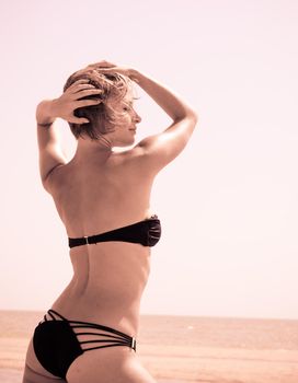 Beautiful red woman wearing bikini standing on the beach enjoying the sun
