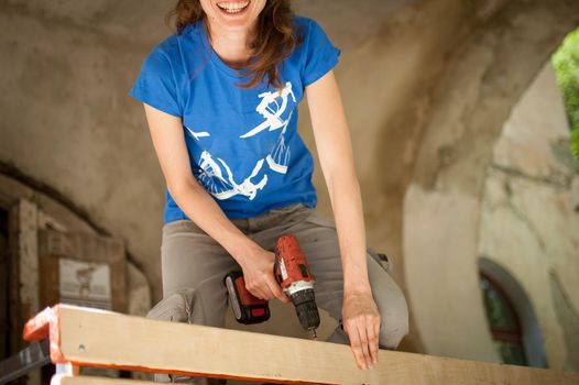 Skilled young female worker is using power screwdriver drilling during construction wooden bench gender equality, feminism, do it yourself concepts
