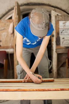Female hands are making some marks on wooden plank for future holes using pencil for assembling bench, gender equality, feminism, do it yourself concepts