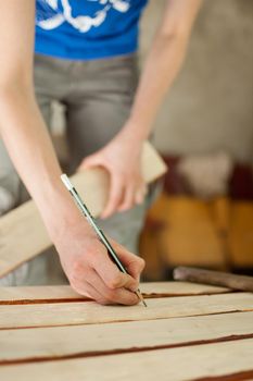 Female hands are making some marks on wooden plank for future holes using pencil for assembling bench, gender equality, feminism, do it yourself concepts