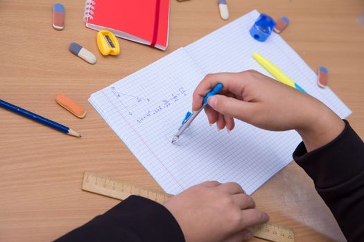 A student in a notebook draws a circle with a compass. A schoolboy performs a task at the workplace. The concept of children's education, teaching knowledge, skills and abilities.