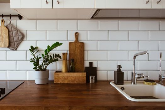 Kitchen brass utensils, chef accessories. Hanging kitchen with white tiles wall and wood tabletop.Green plant on kitchen background side view