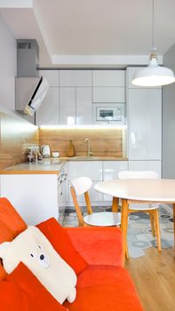 Modern kitchen interior with wooden and white elements, bright orange sofa, domestic life, home showcase interior concept