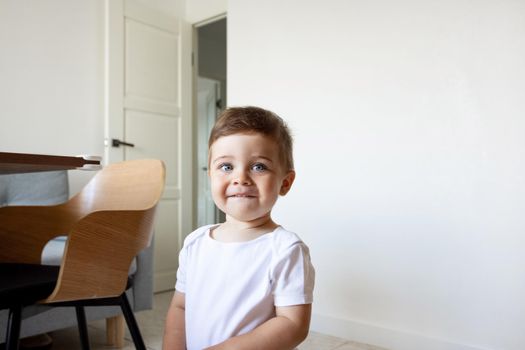 Funny happy healthy toddler sitting at the kitchen at home, pretty eyes, kids play and childhood side view