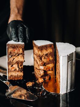 Amazing Cakes. A black-gloved chef is slicing a chocolate wedding cake. The wedding Cake is delicious inside on a black background.Large cake in white chocolate