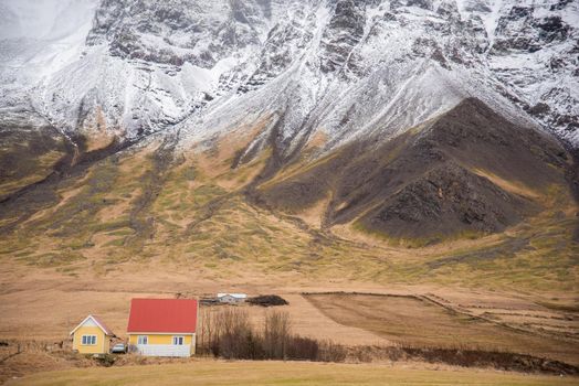 Iceland scene with red roof cottage with huge snow capped mountain in the background snow creates texture black grey green brown