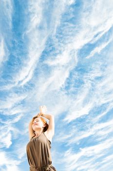 Beautiful young dancer performing yoga-dance outdoors with blue sky and clouds in the background