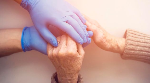 A doctor's hands in a blue gloves holds the hands of an elderly woman, a patient. Handshake, caring, trust and support. Medicine and healthcare.