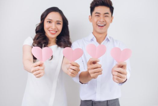 Happy young Vietnamese couple is holding pink paper hearts and smiling